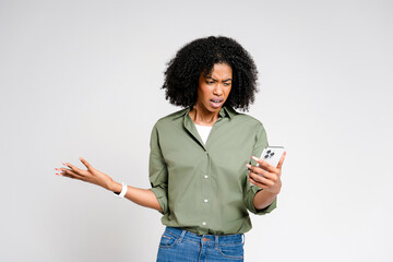 Surprised and slightly perplexed, this African-American woman looks at her smartphone screen, her expression mixing confusion with curiosity, set against a minimalist white background.