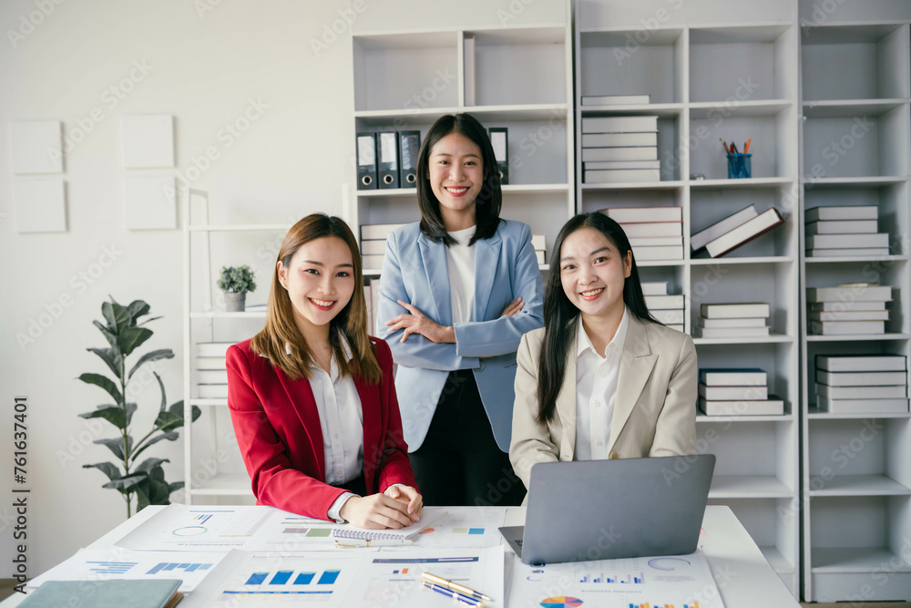 Poster three women in business attire pose for a photo in front of a bookshelf