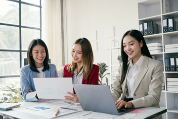 Three women are sitting at a table with laptops and papers