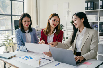 Fototapeta premium Three women are sitting at a table with papers and laptops