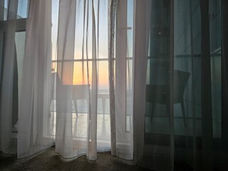 Window is open in house, evening light fills room of apartment, bright ray of sun shines through window, wind stirs curtain