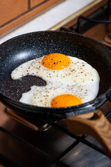 two fried eggs in a frying pan on the kitchen stove, vertical