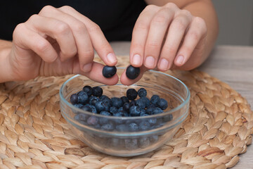Fresh Blueberries in a Glass Bowl in Female Hands. Picking ripe blueberries from a glass bowl.