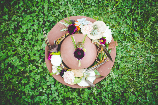 Trendy Floral Bridal Hat Lying on Clover: Bohemian Spring Aesthetic Photograph of Wide Brim Hat Lying on Ground in the Middle of Weeds with Boho Flower Crown