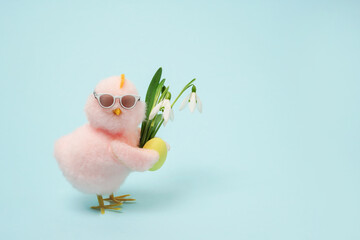 small cool chick in sunglasses with Easter egg and flowers on blue background, copy space