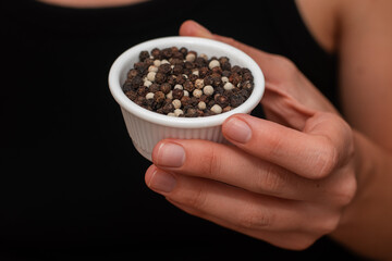 Bowl of Whole Peppercorns in a Female Hand. Gently holding a ramekin filled with assorted whole peppercorns.