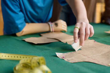 Close up of unrecognizable girl with disability making clothing and tracing patterns in sewing...