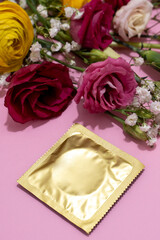 Golden wrapped condom alongside a delicate flowers on pink background