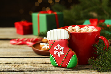 Tasty cookie in shape of Christmas stocking, cocoa with marshmallows and fir tree branch on wooden table, closeup. Space for text