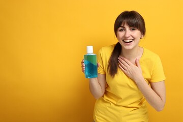 Young woman with mouthwash on yellow background, space for text