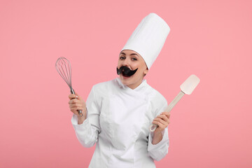 Funny professional confectioner in uniform holding whisk and spatula on pink background