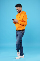 Happy young man using smartphone on light blue background