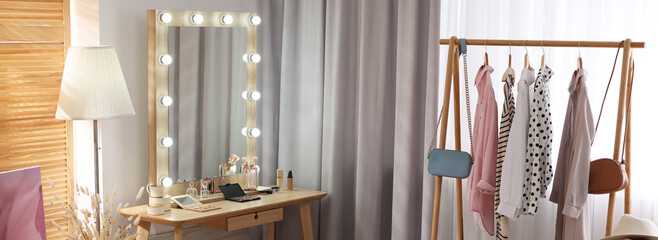 Makeup room. Stylish dressing table with mirror, chair and clothing rack indoors, banner design