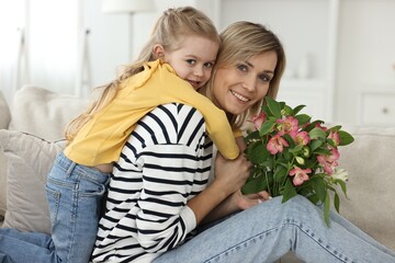 Little daughter congratulating her mom with Mother`s Day at home. Woman holding bouquet of...