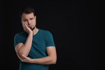 Portrait of sad man on black background, space for text