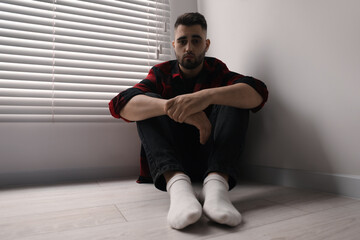 Sad man sitting on floor at home, low angle view