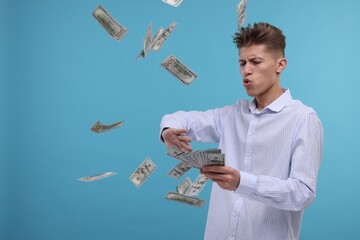 Handsome man throwing dollar banknotes on light blue background