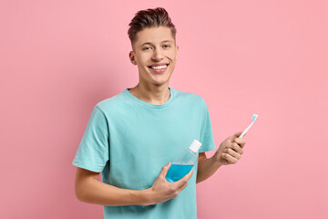 Young man with mouthwash and toothbrush on pink background - obrazy, fototapety, plakaty
