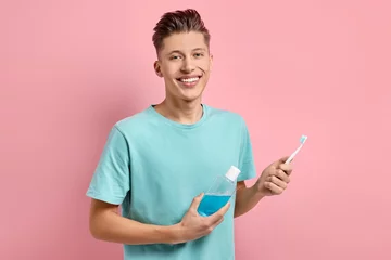 Gardinen Young man with mouthwash and toothbrush on pink background © New Africa