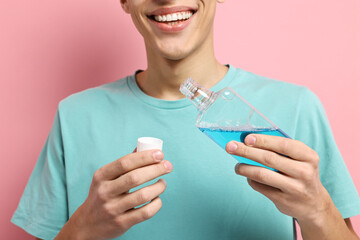Young man using mouthwash on pink background, closeup