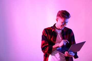 Young man with laptop talking via video chat on pink background in neon lights. Space for text