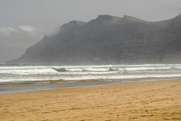 View of the wavy ocean and cliffs in the Famara beach in a sunny day with a light haze in the air, Lanzarote, Canary Islands