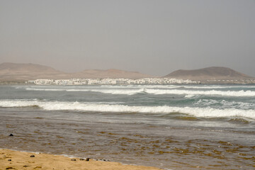 View of the wavy ocean and cliffs in the Famara beach in a sunny day with a light haze in the air, Lanzarote, Canary Islands