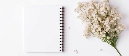 A ring binder and a sketch pad, placed next to a bouquet of white flowers, create a beautiful composition on a white background. A mix of office supplies and plant decor