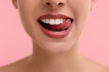 Woman with beautiful lips licking her teeth on pink background, closeup