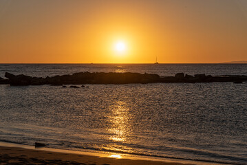 Orange sunset over ocean and reef with boat on horizon - 761669648