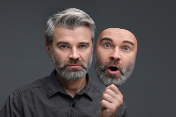 Man holding mask with his facial expression on grey background. Personality crisis, different emotions