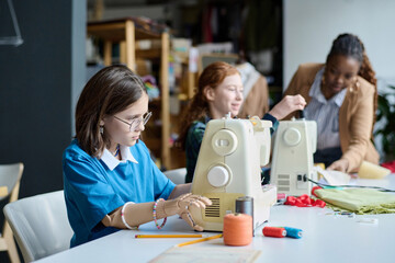 Side view portrait of girl with prosthetic hand using sewing machine in tailoring class