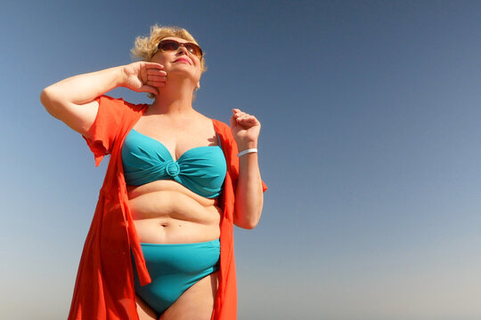 Senior woman wiping the sweat from his forehead with a towel in sea beach, abnormal heat dangerous to health, outdoors