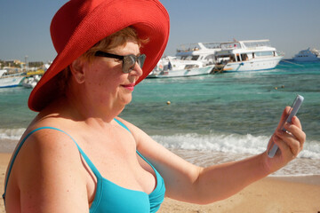Senior adventure is ageless plus size woman wearing in swimsuit speak by mobile phone on the beach. Summer vacation for pensioner.