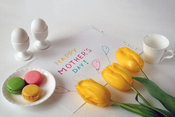 preparing a festive breakfast for mother's day with french macarons, eggs postcard, flowers and gifts, happy mother's day