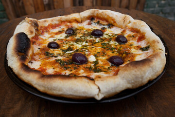 Traditional pizza. Closeup view of a mozzarella cheese pizza with tomato sauce, black olives and fresh oregano, on the wooden table.	
