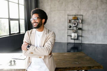 Young businessman in a beige suit strikes a pose with his arms confidently crossed, reflecting a...
