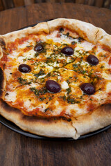 Traditional pizza. Top view of a mozzarella cheese pizza with tomato sauce, black olives and fresh oregano, on the wooden table.	
