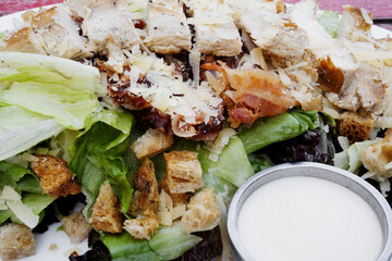 Caesar salad background. Top view of a fresh salad with lettuce, parmesan cheese, bread croutons, sliced grilled chicken breast, bacon and Caesar dressing.	