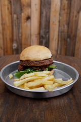 Plant based food. Vegetarian burger. Closeup view of a NotCo burger with potato bread, mushrooms, sun dried tomatoes, arugula and NotCo mayonnaise, in a metal dish on the restaurant wooden table.	
