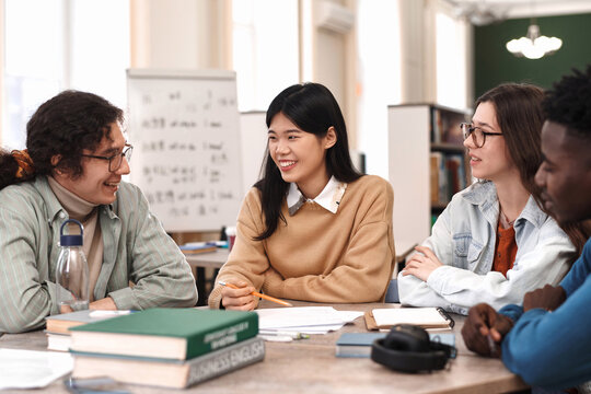 Diverse group of young people studying together sitting at table in college library and discussing schoolwork - Powered by Adobe