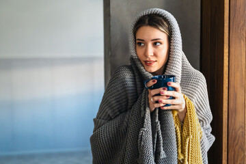 Tired and sick woman is covered with a blanket holding a cup of hot drink, medicine.Cold flu concept