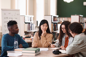 International group of students sitting at table in college library and studying together with focus on young Asian woman