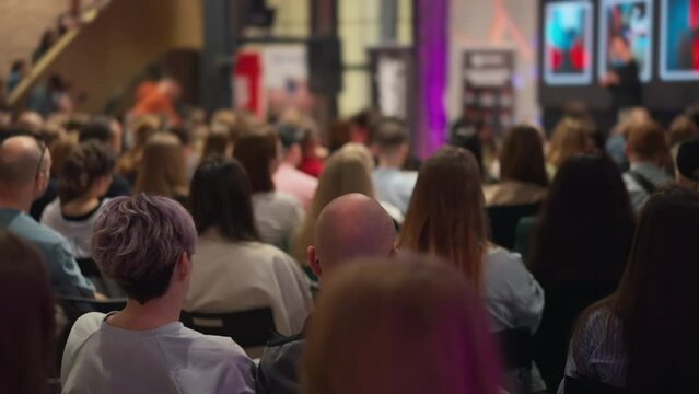 Girl with colored hair among audience of young innovators absorbed in tech presentation, foregrounding interaction, speaker in background. Reflects dynamism of technology and innovation conferences