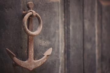 wooden door with an iron knocker in the shape of an anchor. old anchor-shaped door handle on a weathered door. 