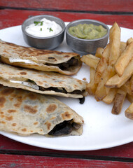 Mexican cuisine. Closeup view of quesadillas filled with cheese, french fries and dipping sauces, in a white dish on the restaurant wooden table	
