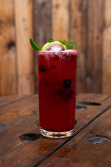 Tropical cocktails. Closeup view of a red berries daiquiri with lime and fresh mint leaves and a rustic wooden background. 