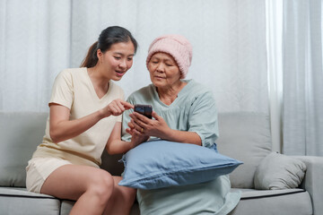 Joy emanates from an elderly Asian lady in teal attire and young adult, both focused on cellular...