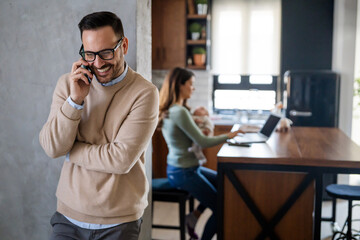 Mother with infant baby working at home on laptop while husband consulting partners by phone