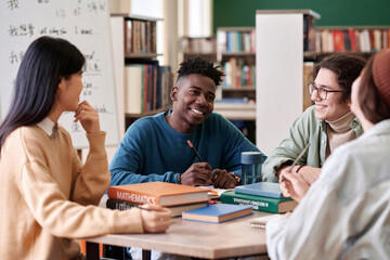 Portrait of Black young man smiling during group discussion with students in college library